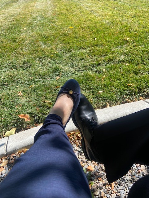 Two feet coming together in sunshine, with green grass, curb and gravel as background