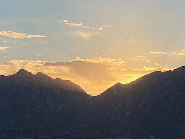 Brighter yellow sunrise coming over the mountains with white clouds in blue sky